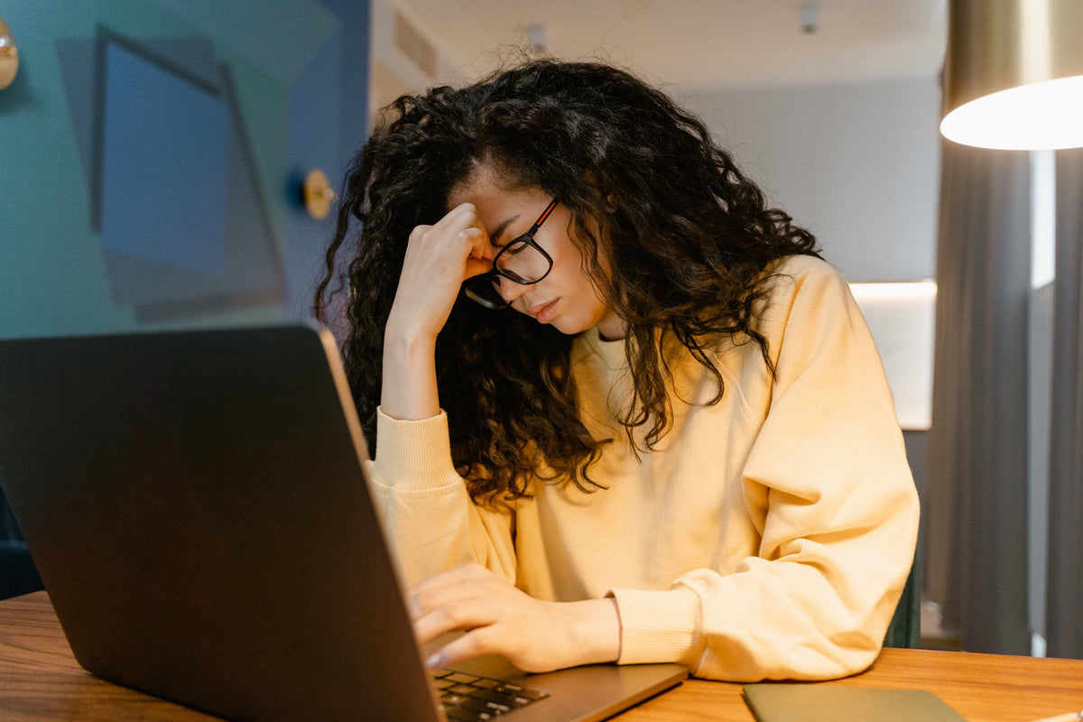 Erschöpfte Frau mit Brille stützt am Laptop den Kopf in die Hand